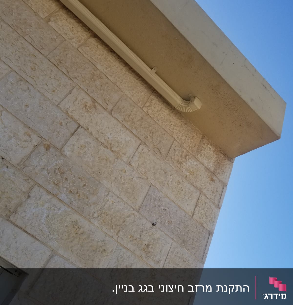 מרזב לבן מחובר לגג בטון על קיר אבן